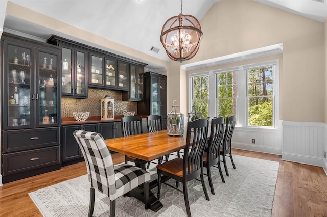 dining area with lofted ceiling, bar, an inviting chandelier, and light hardwood / wood-style floors