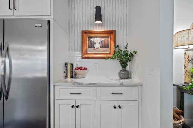 bar featuring white cabinetry, stainless steel fridge, light stone countertops, and backsplash