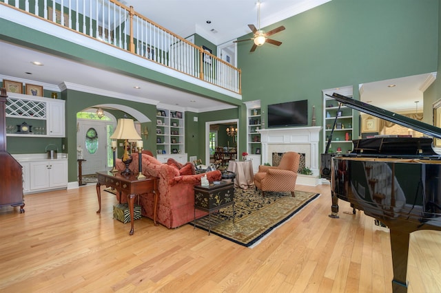 1811 Snug Harbor Dr, Greensboro, GA 30642 - living room featuring a towering ceiling, light wood-style flooring, a fireplace with raised hearth, a ceiling fan, and crown molding