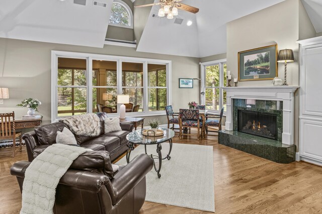 living room featuring ceiling fan, a premium fireplace, high vaulted ceiling, and light wood-type flooring