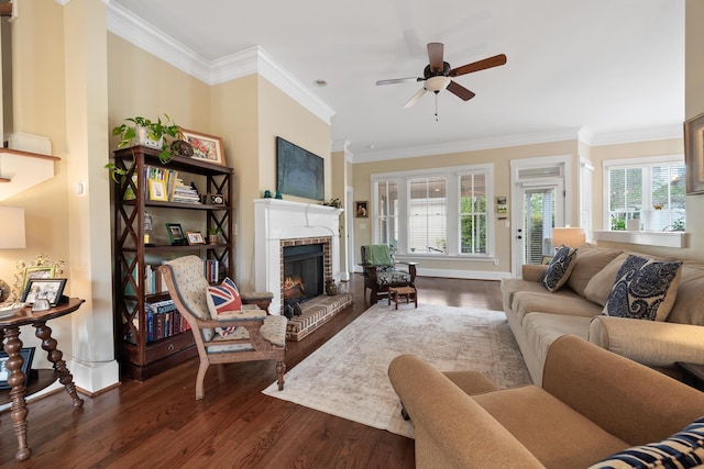 living area featuring dark wood-style flooring, ornamental molding, ceiling fan, and a brick fireplace