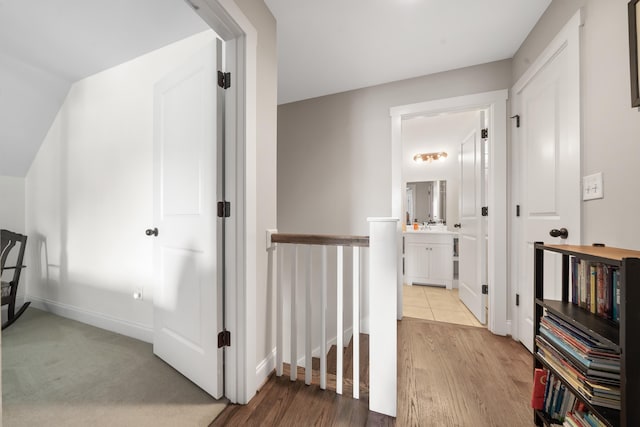 corridor with baseboards, an upstairs landing, and wood finished floors
