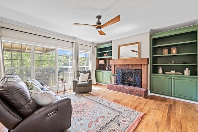 living room featuring built in shelves, a brick fireplace, ornamental molding, ceiling fan, and hardwood / wood-style floors