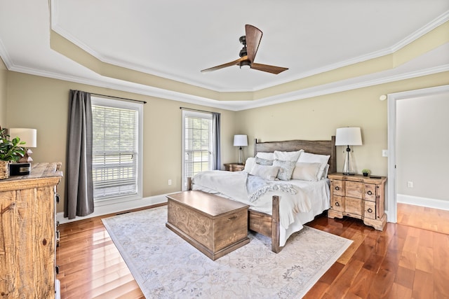 bedroom with crown molding, ceiling fan, wood-type flooring, and a raised ceiling