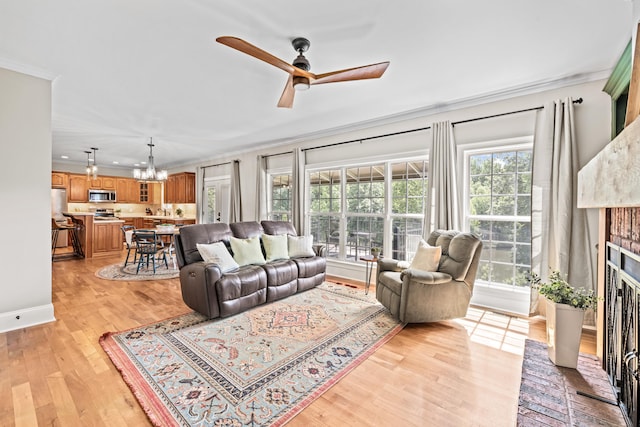 living room with crown molding, a brick fireplace, ceiling fan with notable chandelier, and light hardwood / wood-style flooring