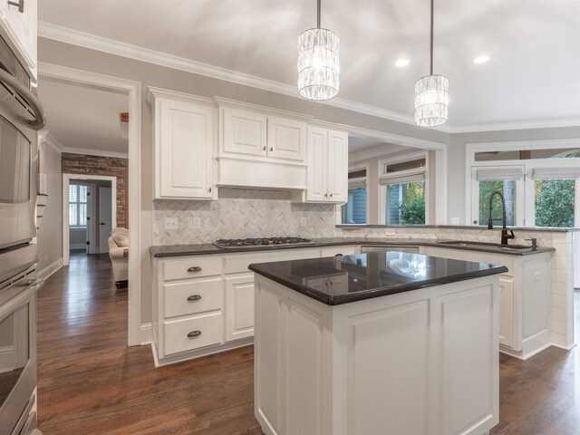 kitchen with white cabinetry, hanging light fixtures, ornamental molding, appliances with stainless steel finishes, and a kitchen island