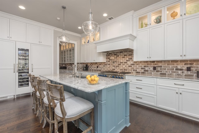 kitchen with white cabinetry, light stone counters, an island with sink, pendant lighting, and decorative backsplash