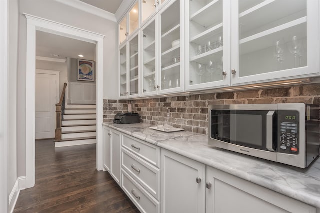 kitchen featuring dark hardwood / wood-style floors, tasteful backsplash, white cabinets, ornamental molding, and light stone countertops