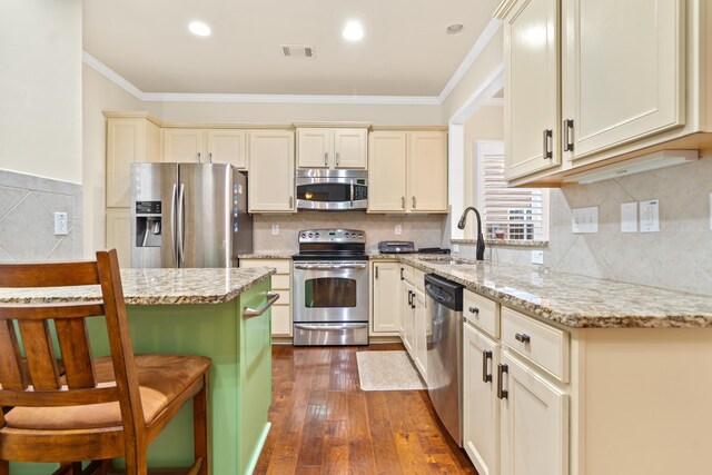 kitchen featuring cream cabinets, stainless steel appliances, sink, and light stone countertops