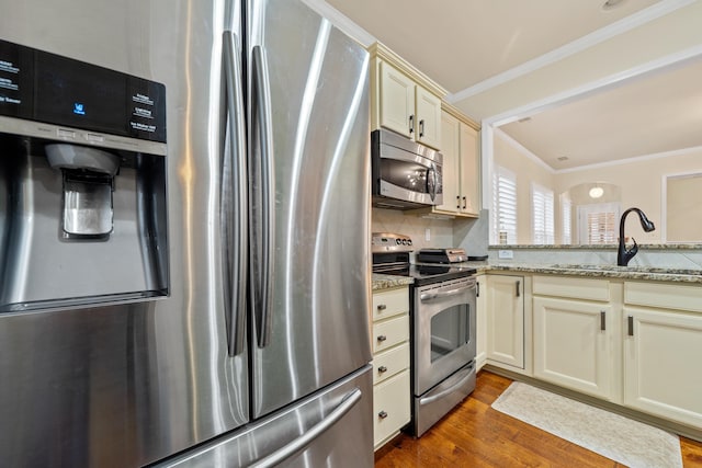 kitchen with sink, stainless steel appliances, cream cabinets, ornamental molding, and light stone countertops