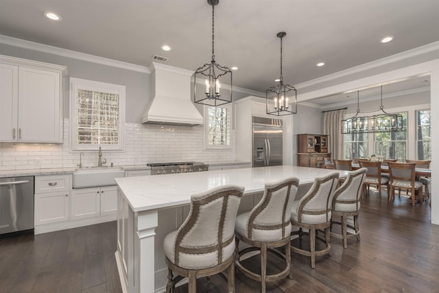 kitchen featuring a kitchen island, a sink, visible vents, appliances with stainless steel finishes, and custom range hood