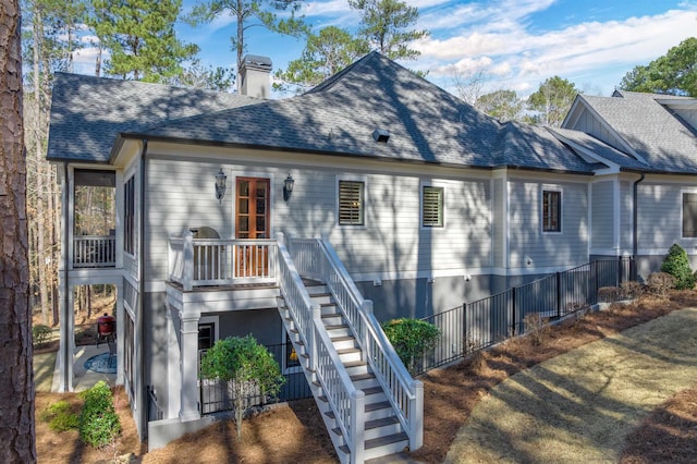 back of house with stairs, a chimney, a patio, and roof with shingles