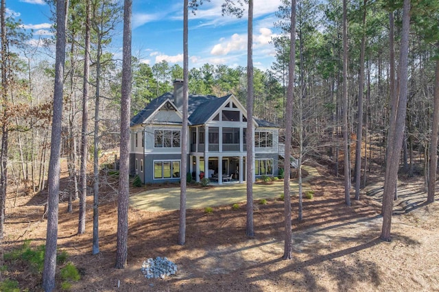 back of property featuring a chimney, a sunroom, and a view of trees