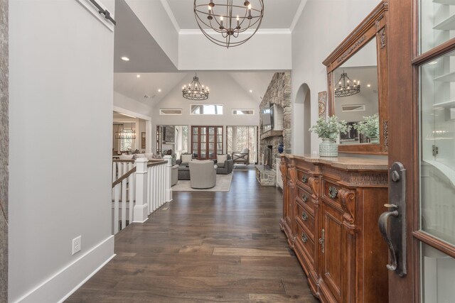 foyer entrance with a chandelier, dark wood-style flooring, crown molding, and a stone fireplace