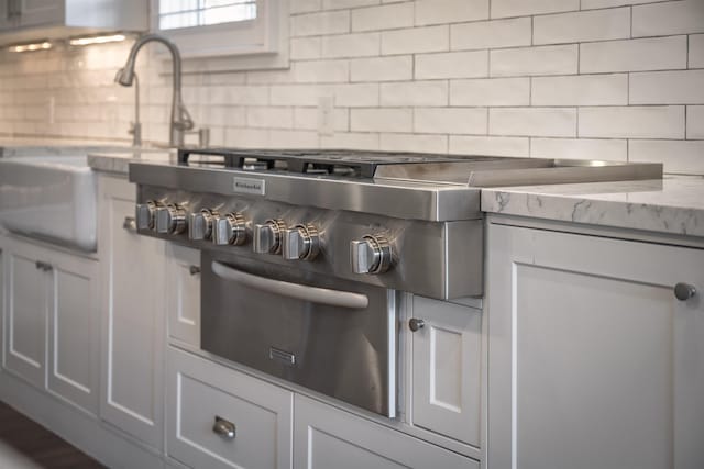 interior details with light stone counters, stainless steel gas cooktop, tasteful backsplash, white cabinetry, and a sink