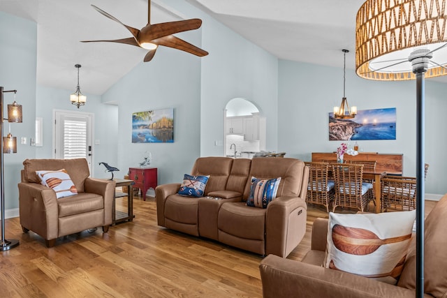 living area with light wood-type flooring, high vaulted ceiling, ceiling fan with notable chandelier, arched walkways, and baseboards