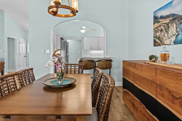 dining room with wood finished floors, baseboards, arched walkways, vaulted ceiling, and ceiling fan with notable chandelier