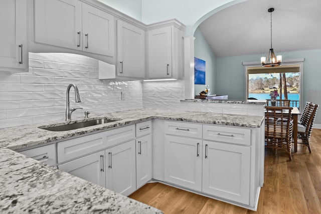 kitchen featuring an inviting chandelier, light wood-style flooring, a peninsula, a sink, and white cabinets