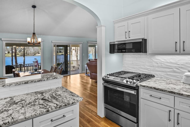 kitchen featuring arched walkways, stainless steel appliances, tasteful backsplash, light wood-type flooring, and a chandelier