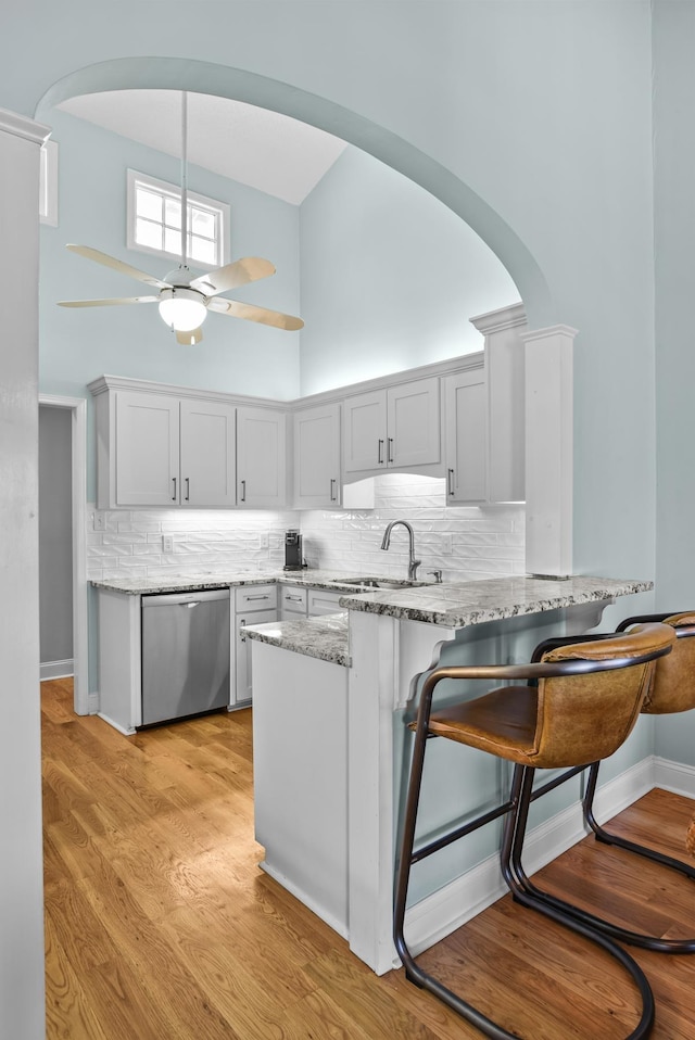 kitchen with a sink, light stone counters, arched walkways, dishwasher, and ceiling fan