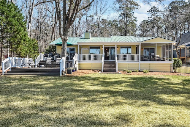 rear view of property featuring a chimney, metal roof, a yard, a sunroom, and a standing seam roof