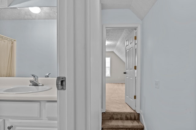 full bath with a textured ceiling, vanity, and lofted ceiling