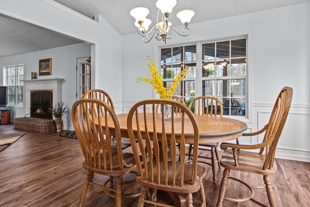 dining space with wood finished floors, an inviting chandelier, a fireplace, wainscoting, and a decorative wall