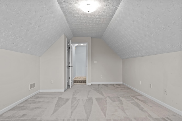 bonus room featuring visible vents, lofted ceiling, a textured ceiling, baseboards, and light colored carpet