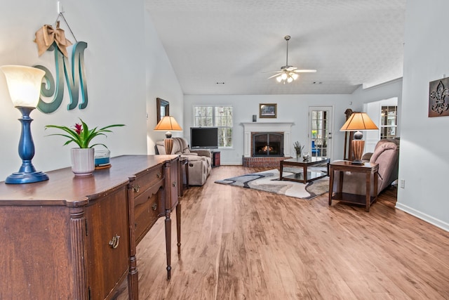 living room featuring light wood finished floors, a fireplace, a ceiling fan, and vaulted ceiling