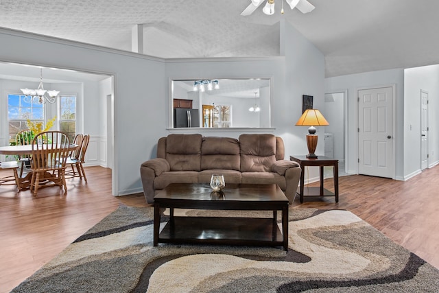 living area featuring vaulted ceiling, wood finished floors, ceiling fan with notable chandelier, and a textured ceiling