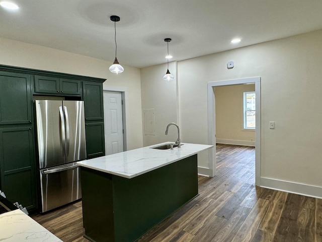 kitchen featuring sink, light stone counters, stainless steel fridge, pendant lighting, and a kitchen island with sink