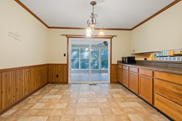 kitchen featuring ornamental molding, wooden walls, ceiling fan with notable chandelier, and hanging light fixtures