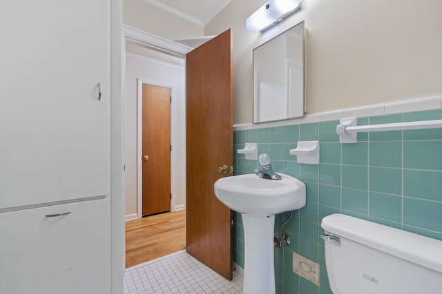 bathroom with tile patterned floors, toilet, sink, crown molding, and tile walls