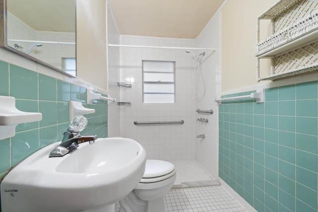 bathroom with toilet, sink, tile walls, a tile shower, and tile patterned flooring