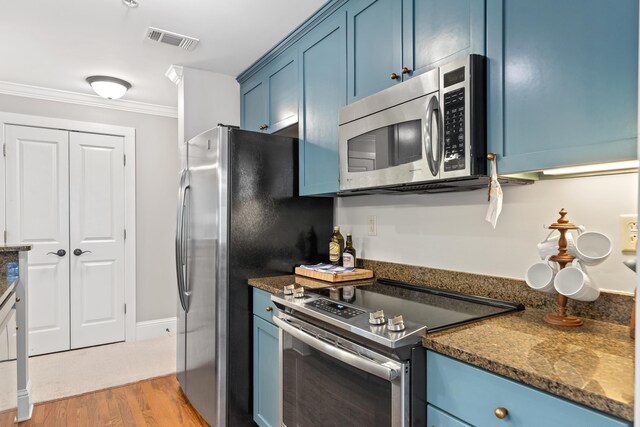 kitchen with crown molding, stainless steel appliances, light hardwood / wood-style floors, blue cabinets, and dark stone counters