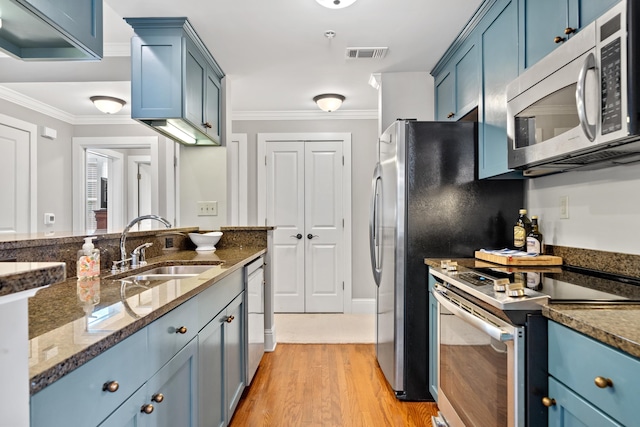 kitchen with appliances with stainless steel finishes, sink, dark stone counters, ornamental molding, and blue cabinetry