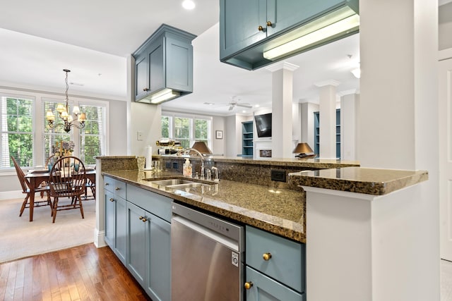 kitchen featuring sink, dishwasher, ceiling fan with notable chandelier, dark stone counters, and ornate columns