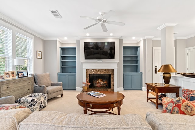 carpeted living room with ornamental molding, built in features, ceiling fan, a premium fireplace, and decorative columns