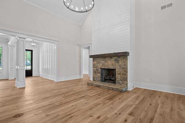 unfurnished living room featuring an inviting chandelier, a stone fireplace, light hardwood / wood-style flooring, and high vaulted ceiling