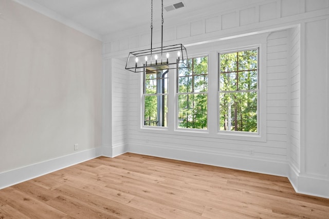 unfurnished dining area with crown molding, light wood-type flooring, a chandelier, and a healthy amount of sunlight