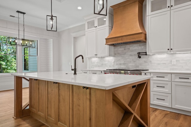 kitchen featuring white cabinetry, custom exhaust hood, and an island with sink