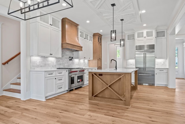 kitchen with white cabinetry, an island with sink, custom range hood, and high quality appliances