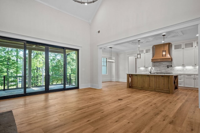 kitchen with premium range hood, decorative light fixtures, a kitchen island with sink, decorative backsplash, and white cabinets