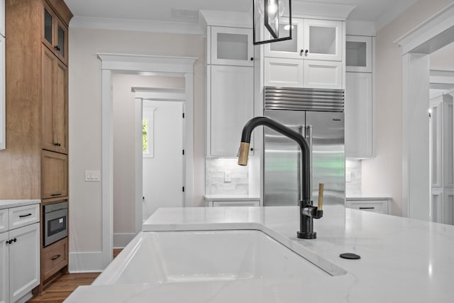 kitchen with built in fridge, pendant lighting, backsplash, white cabinets, and light stone counters