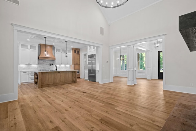 unfurnished living room featuring sink, a notable chandelier, high vaulted ceiling, and light hardwood / wood-style flooring