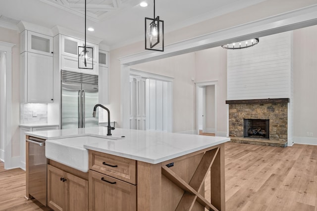 kitchen with pendant lighting, appliances with stainless steel finishes, white cabinetry, ornamental molding, and a center island with sink