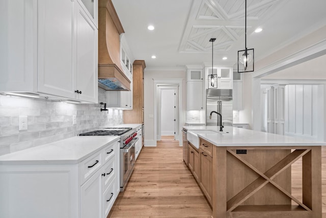 kitchen featuring hanging light fixtures, premium appliances, custom range hood, white cabinets, and a large island with sink