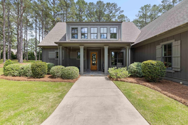entrance to property featuring board and batten siding, covered porch, roof with shingles, and a yard