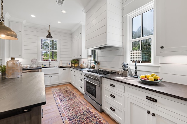 kitchen featuring high end stainless steel range, dark countertops, visible vents, a sink, and white cabinetry