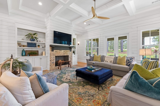 living room with beam ceiling, coffered ceiling, wood walls, a brick fireplace, and ceiling fan